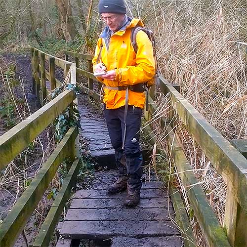 An footpath inspector writing in a booklet about broken boards on a boardwalk