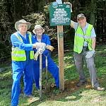 Three volunteers proudly posing next to the signpost they've just planted