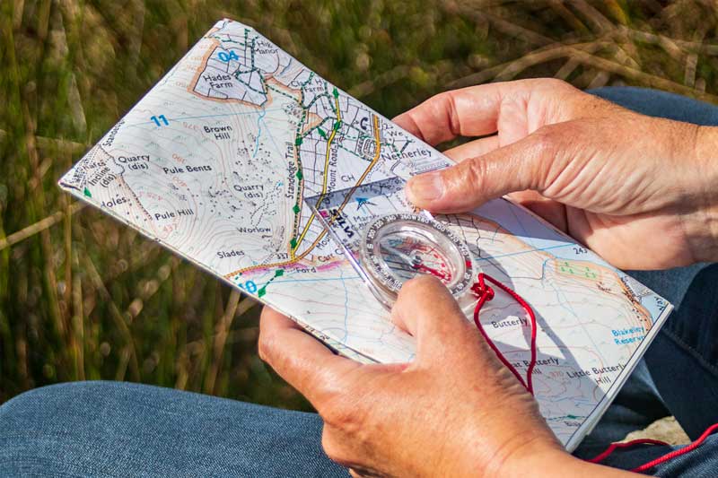 Two hands holding an Ordnance Survey map and a compass
