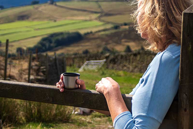 Someone leaning on a gate with a cup of tea looking at the scenery