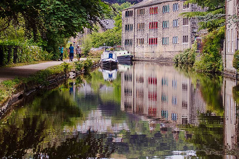 A group of walkers by a canal with warehouses reflected in the water